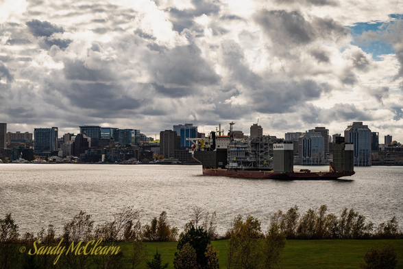 Semi-submersible heavy-lift vessel in a harbour under a partly cloudy sky with cargo embarked.