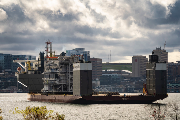 Semi-submersible heavy-lift vessel in a harbour under a partly cloudy sky with cargo embarked