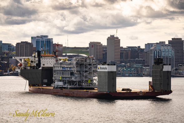 Semi-submersible heavy-lift vessel in a harbour under a partly cloudy sky with cargo embarked