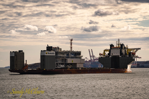 Semi-submersible heavy-lift vessel in a harbour under a partly cloudy sky with cargo embarked