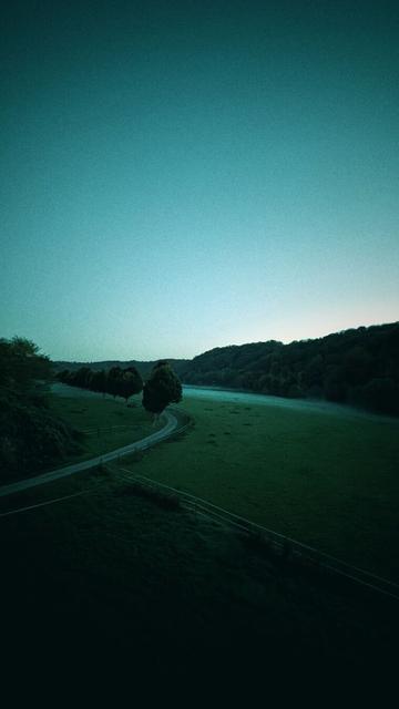A serene landscape bathed in a cool, blue light, showcasing a winding road, a tranquil river, and a backdrop of rolling hills.