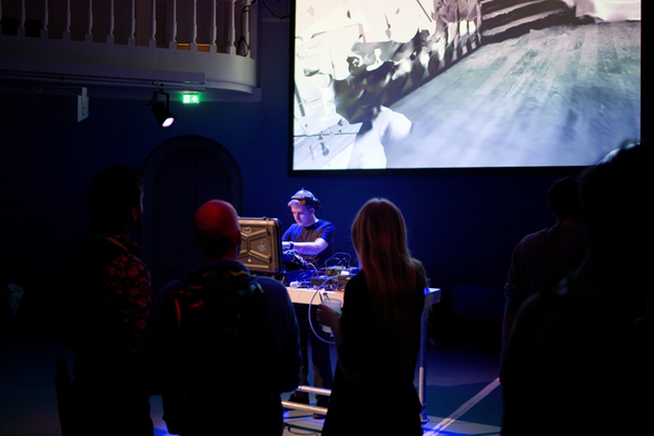 Me performing in the Felix Meritis Studio Room with people listening in the foreground and a 3D Scan of the Felix Meritis stairs as 3D scan