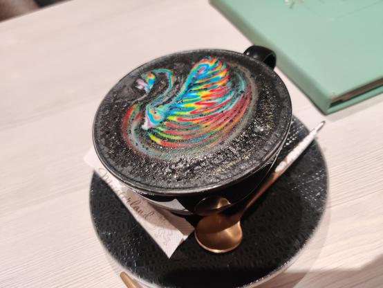 Schwarzer Cappuccino mit Schwan in regenbogenglitzer
