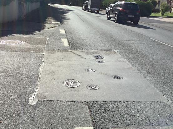 Holpriger Straßenrand mit kleinen runden Kanaldeckeln, leicht abgesenkt