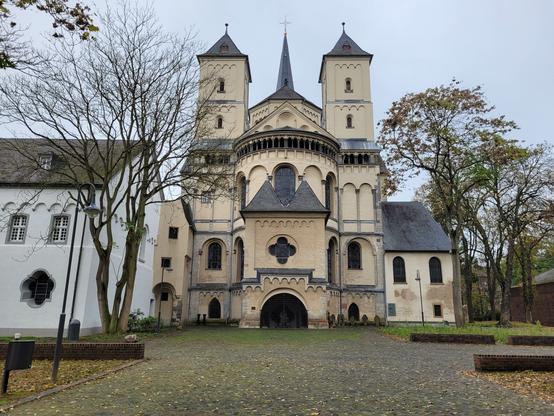 Die Abteikirche "von hinten": eunde romanische Apsis mit zwei eckigen Türmen links und rechts, weiter hinten die Spitze eines massiven Vierungsturms. Links von der Kirche Teile des Klosterbaus mit Kapitelsaal im Erdgeschoss und Dormitorium darüber sichtbar.