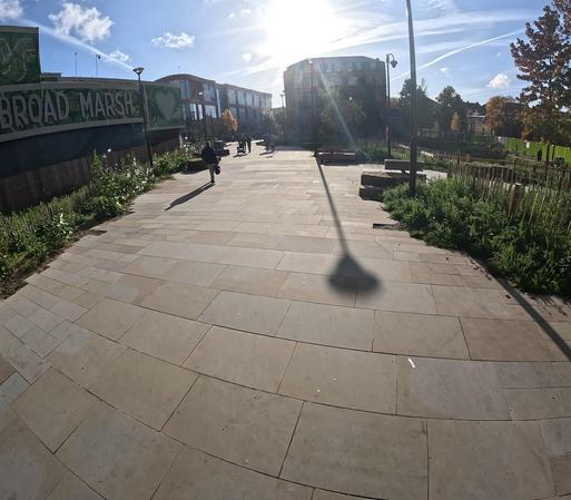 Urbo centro ĝardeno. Strateto iras tra la ĝardeno. La ĉielo estas blua, la suno brilas