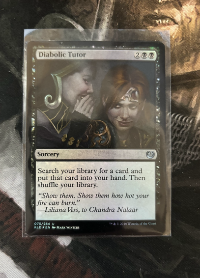 A foil Magic: the Gathering card from the Kaladesh expansion: Diabolic Tutor, 2BB, Sorcery Search your library for a card, put that card into your hand, then shuffle. “Show them. Show them how hot your fire can burn.” —Liliana Vess, to Chandra Nalaar
