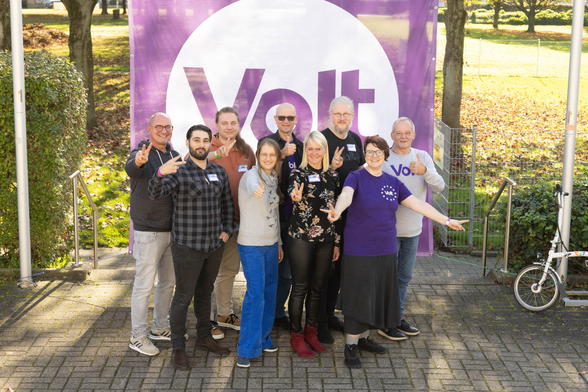 Ein Teil des Teams von Volt Essen, wie es vor einem großen Volt-Banner in die Kamera lacht.