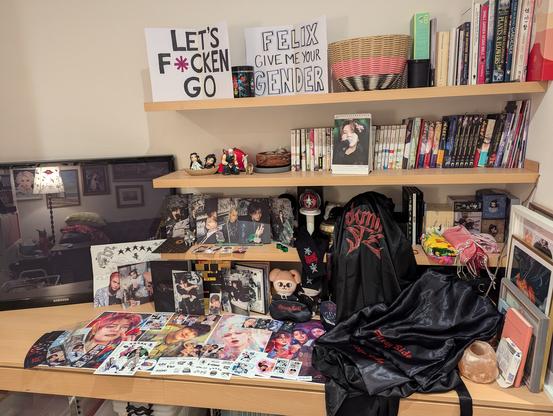 A wider shot of the stray kids merch and the surrounding shelves. Two hand-made signs are on the top shelf.