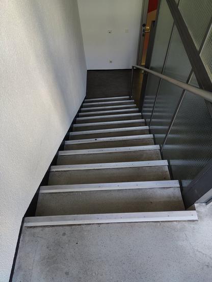 Foto einer Treppe, von oben nach unten aufgenommen. Die Stufen sind nicht parallel, unterschiedlich tief und auch nicht rechtwinklich zur Wand.