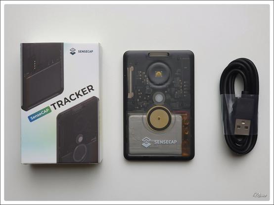 Bildbeschreibung:
Auf einem weißen Tisch liegen von links nach rechts, die Verpackung des SenseCAP, der scheckkartengroße SenseCAP selber und daneben das USB-Kabel.