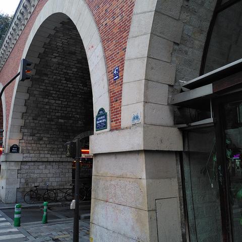 Une mosaïque bleue et grise représentant un space invader, collée sur une arche de pierre et de briques.