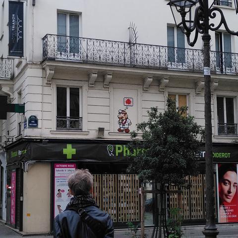 Une mosaïque blanche et rouge représentant un Mario (?) déguisé en médecin, avec au dessus de lui une bulle représentant un virus de la covid 19.