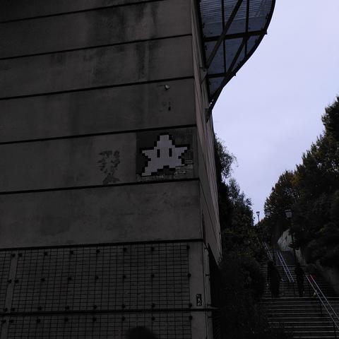 Une mosaïque blanche et grise représentant une étoile du genre de celles qu'on croise dans les jeux vidéo Mario. Son coin inférieur droit s'est décollé.