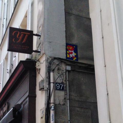 Une mosaïque bleue, blanche et rouge représentant un ninja de jeu vidéo, peut-être issue d'un bomberman ?
Collée sur un mur sombre d'un étroit passage...