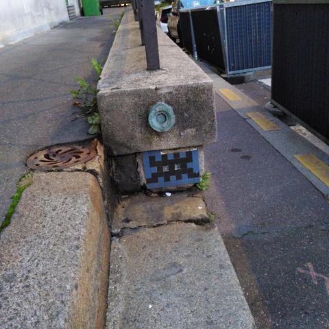 Une mosaïque bleue et noire représentant un space invader, elle est collée au ras du sol près d'un escalier.