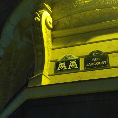 Une mosaïque bleue verte et rouge représentant deux space invader, juste à côté d'une plaque de rue parisienne, avec les mêmes couleurs, le même format, et même un chapeau indiquant "12e Arrt" !