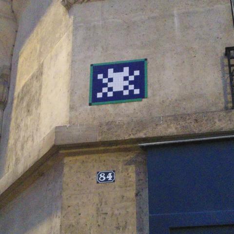 Une mosaïque bleue, verte et blanche représentant un space invader, là aussi dans le style des panneaux de rues parisiennes.
