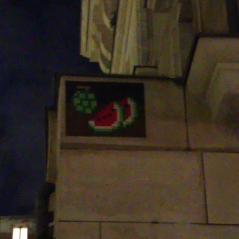 Une mosaïque verte et rouge représentant un deux tranches de pastèque (à la manière des bonus de pac-man) et un fruit vert non identifié.
