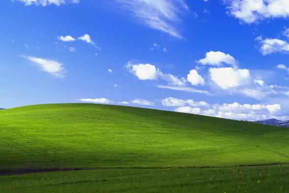 The famous Windows XP screen background with rolling grass-covered hillside, blue sky and small white puffy clouds.