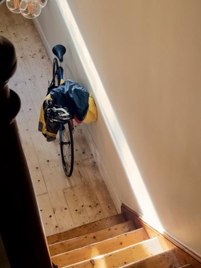A photo taken down a set of interior wooden stairs, at the bottom of which is a vintage road bike covered in rain clothes.