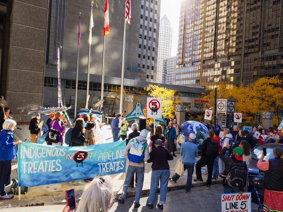 A banner says "Indigenous Treaties Not Pipeline Treaties" in front of a large rally crowd outside the Canadian consulate in downtown Chicago