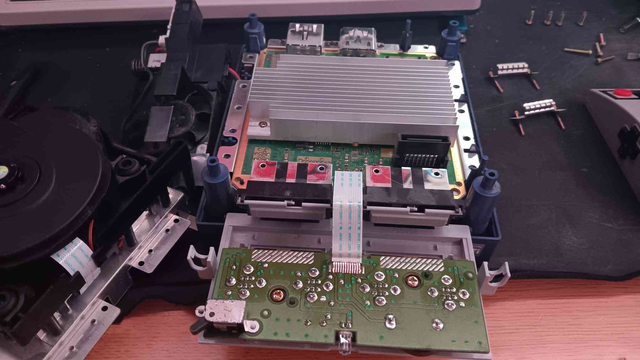 A Nintendo Gamecube. The top shell is off, the Disk Drive has been removed, and the Fan/Power button, and Front IO boards are hanging out