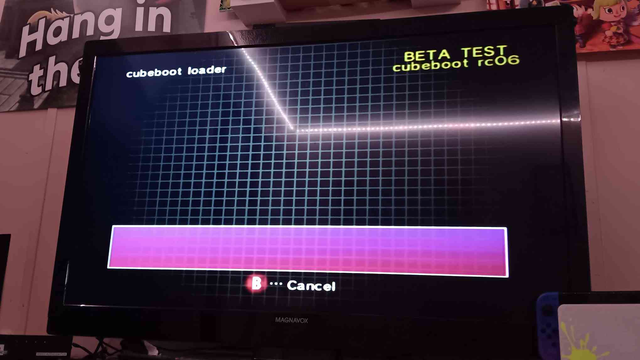 A Gamecube menu showing an empty screen and empty purple box at the bottom. Text at the top left of the screen shows "cubeboot loader," and large yellow text at the top right reads "BETA TEST - cubeboot rc06"