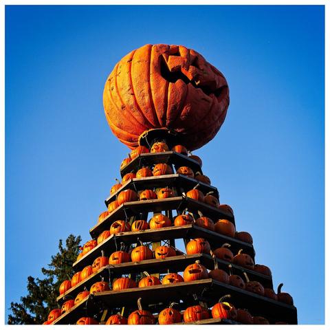A tower of carved pumpkins against a clear blue sky.