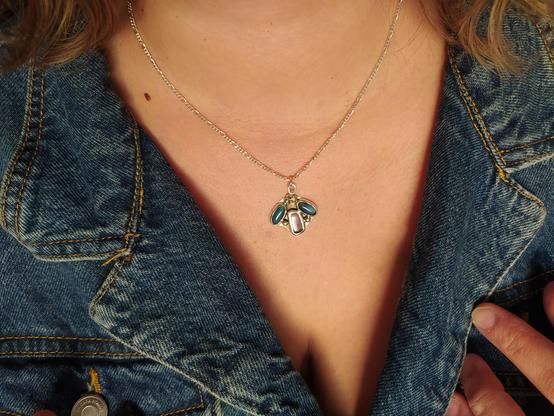 a silver pendant with two oval blue gemstones and one dark transparent. it has a silver chain too. it's worn by a woman with blue denim shirt