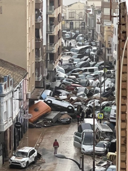 Eine Straße ist in der Flucht zu sehen. Sie ist gefüllt mit angeschwemmten Autos, die sich zu Haufen ballen.