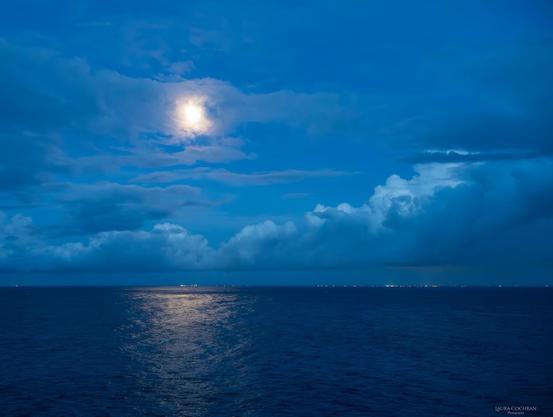 The early morning moon, peaking through the clouds, is reflected in the water below.