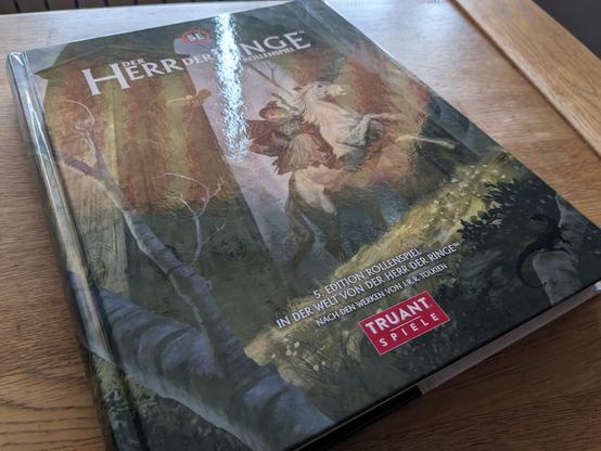 Das Buch liegt auf einem Holztisch. Ungünstige Beluchtung sorgt für Spiegelung auf dem Titel, man kann eine Waldszene mut Gandalf auf einem Pferd erahnen