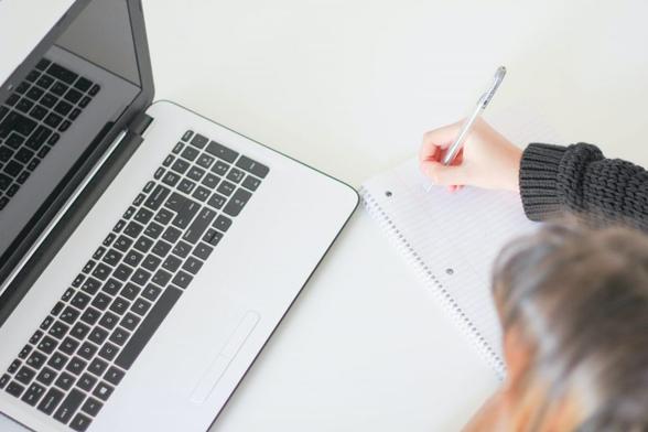 iemand met blocnote en pen voor een laptop