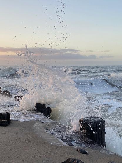 Color image of the Atlantic Ocean meeting the Eastern Carolina seaboard, Edisto Beach, Edisto Island, South Carolina, USA. Image shows a roiling and rough ocean at high tide slamming against the groins built to hold off shoreline erosion. Clear sky above, clouds on the horizon.