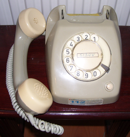A photo of an old rotary dial phone, beige coloured. It's dumbell style receiver is off the hook