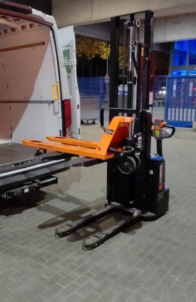 An electric pallet lift truck with a smaller, manual lift truck on its forks