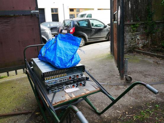 Des serveurs et un SAN posés sur un genre de brouette permettant de les transporter. Le matériel attend à l'extérieur, derrière un grand portail.