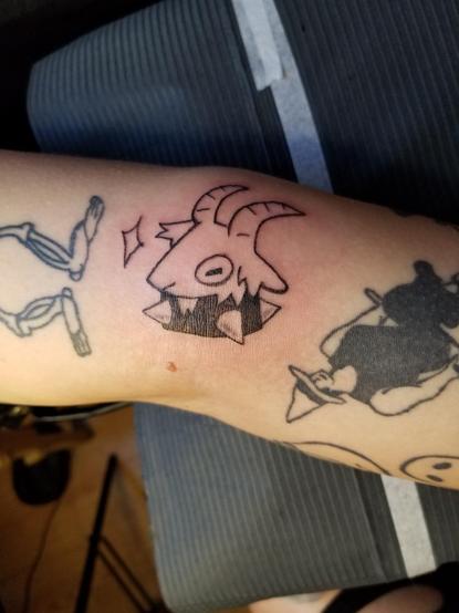 2nd tattoo is another goat, facing up on the other side of the elbow on the same person. Except this goat has a sparkle in front of them, and no flame or upside down star.