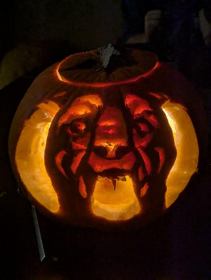 Carved pumpkin showing either the face of a golden retriever or a demon from hell.