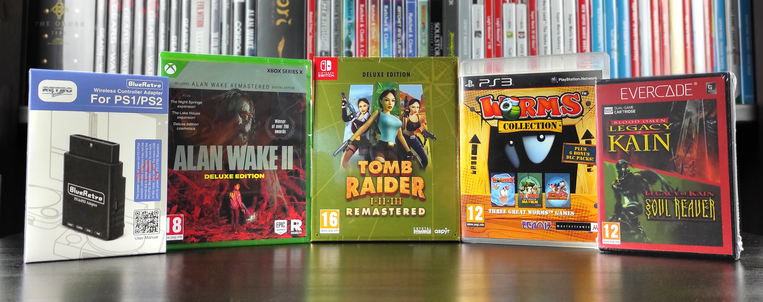 Zdjęcie z comiesięcznymi zdobyczami. Od lewej - pudełko z adapterem bezprzewodowym BlueRetro do konsoli PlayStation oraz PlayStation 2, pudełko z grą "Alan Wake II" w edycji "Deluxe" na konsolę XBOX Series X, pudełko z grą "Tomb Raider I•II•III Remastered" w edycji "Deluxe" na konsolę Nintendo Switch, pudełko ze zbiorczym wydaniem gier z serii "Worms" - "Worms Collection" - na konsolę PlayStation 3 oraz pudełko z kartridżem z grami "Legacy of Kain vol. 1" na konsolę EVERCADE.