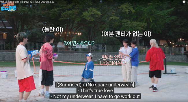 Bang Chan kneels on a volleyball court. Behind him, Han has his arms around Lee Know. Other members of Stray Kids stand around them with water guns and large bowls of water. Captions say: (Surprised) / (No spare underwear) / - That's true love / - Not my underwear, I have to go work out