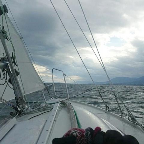 Vue depuis un bateau à voile sous un ciel gris sur un lac. Des montagnes sur la droite.