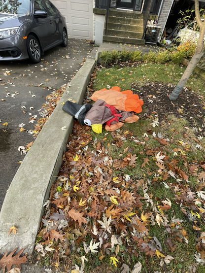 A deflated inflatable turkey wearing a hat flat on the ground looking forlorn.