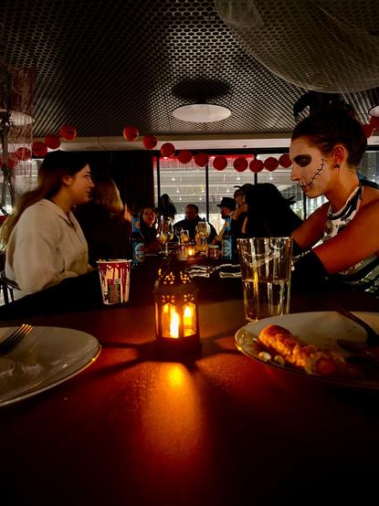 Mehrere Menschen an einer geschmückten Tafel sitzend, manche sind verkleidet, essen und unterhalten sich.
