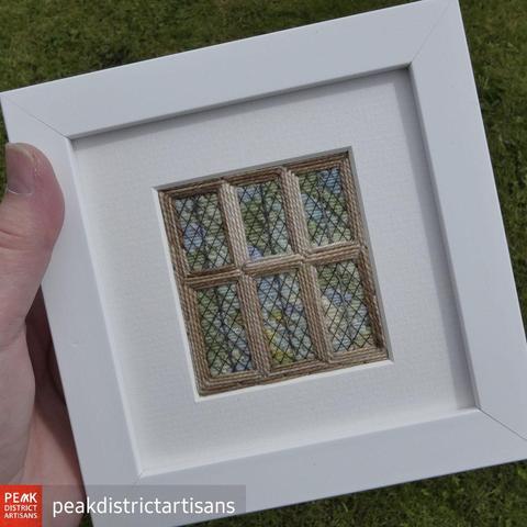 Stitched artwork depicting a mullioned window with 6 leaded galss panes. Framed in a white 5x5 inch frane