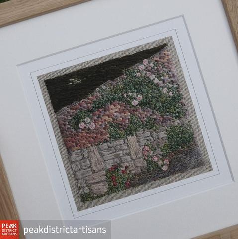 Framed print taken from a stitched artwork depicting climbing roses against a stone and brick wall