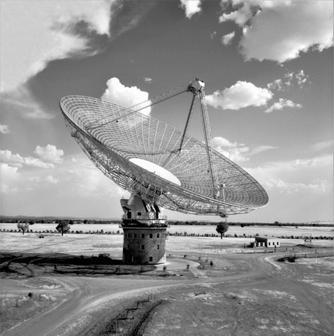 Old black and white image of the Parkes radio telescope in an open field. Taken during the early days of telescope operations.