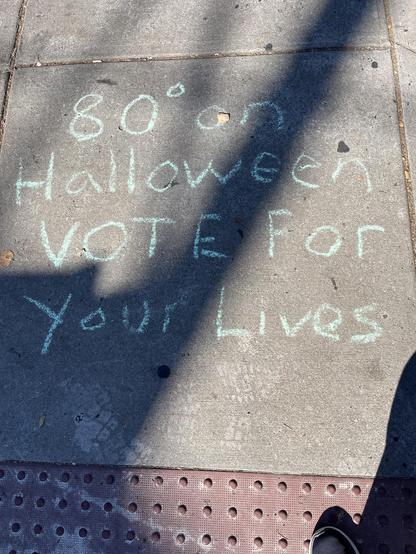 Chalk on a sidewalk: “80 degrees on Halloween VOTE for your lives”