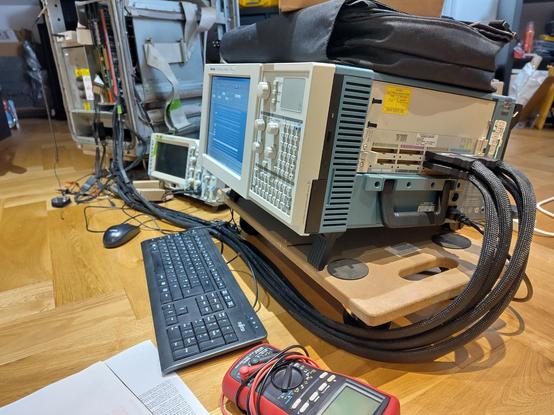 A boxy Tektronix TLA714 logic analyser (basically a box with an LCD on the front) is in the foreground. Four thick cables full of probe wires snake out of the box and back into the PERQ in the background.